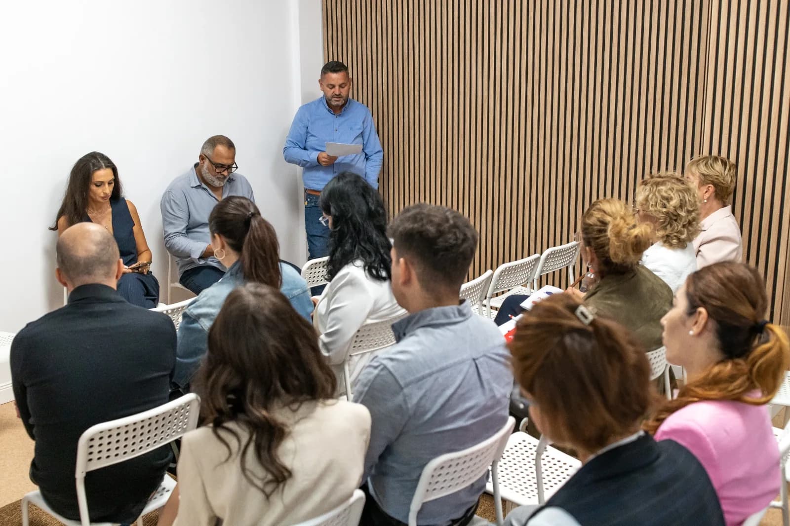 Participanți așezați în sala centrului ascultă un bărbat care vorbește ținând câteva foi.