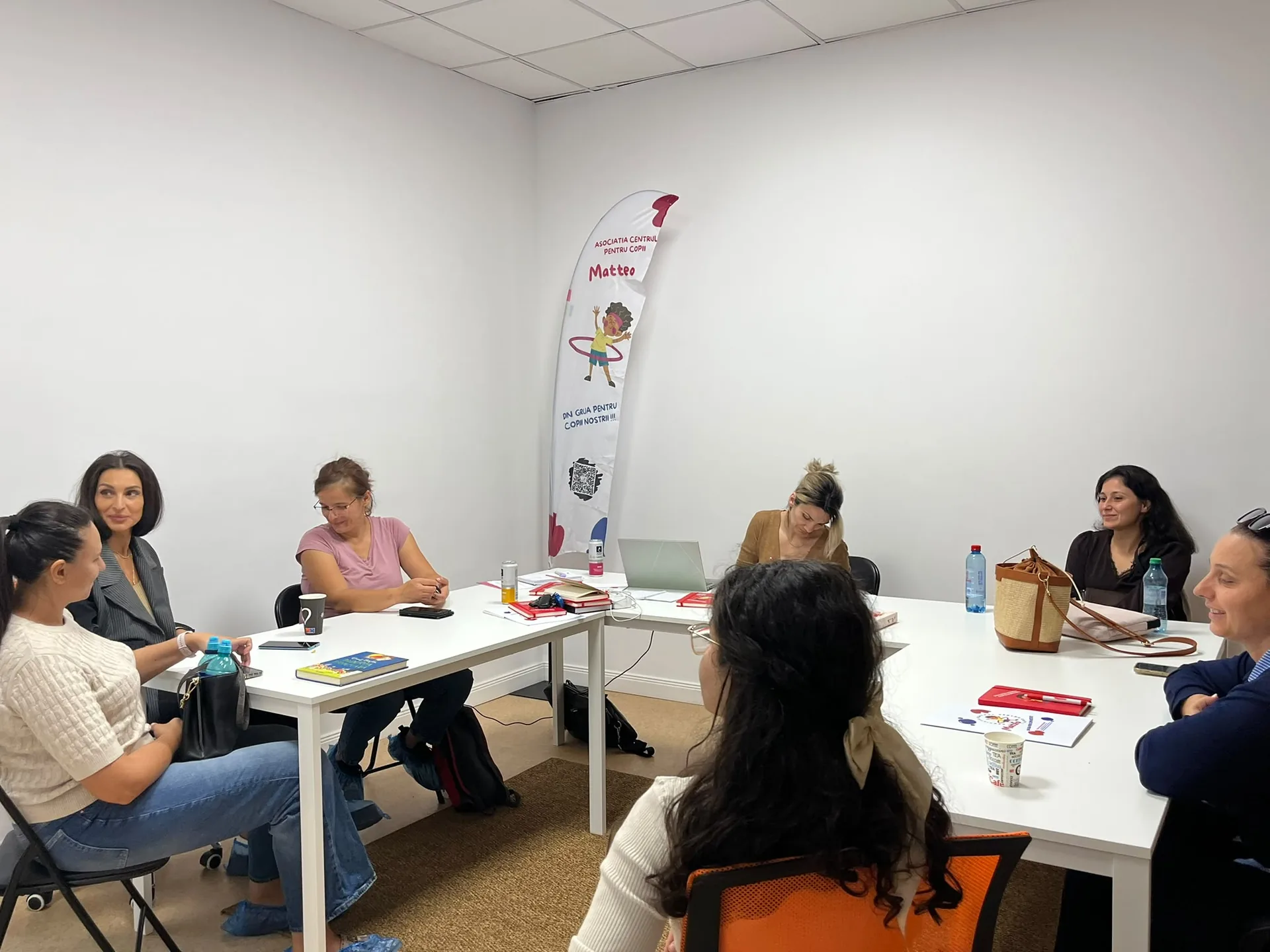 People attending a meeting sit around white tables with materials and notebooks.