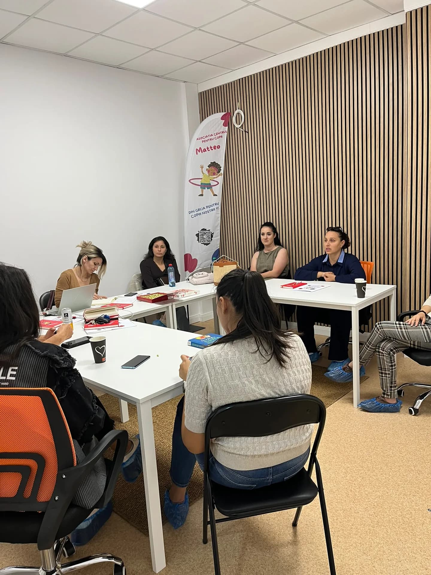 A group of adults talks around white tables beside a Matteo flag and a wooden slat wall.