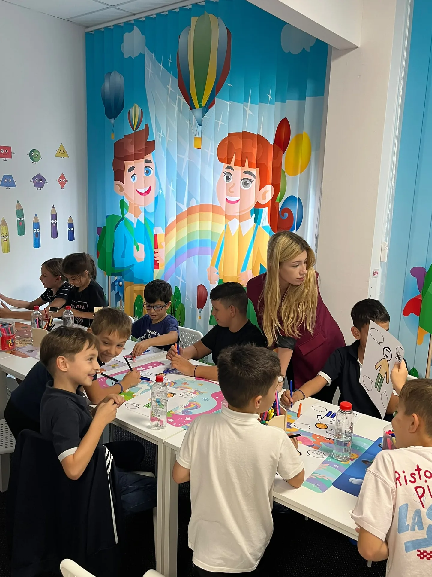 Children draw together while one child holds a colored sheet in front of their face.