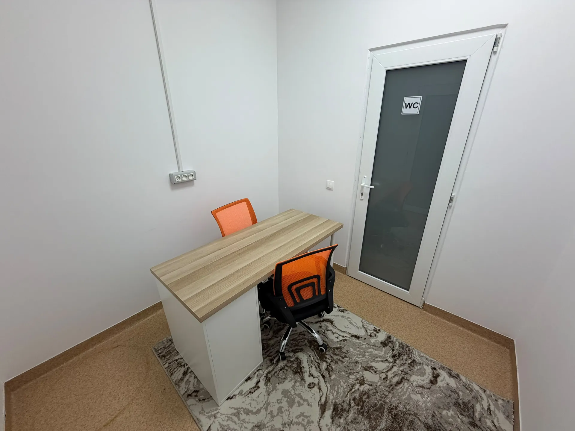 A room with a wooden desk and two orange chairs.