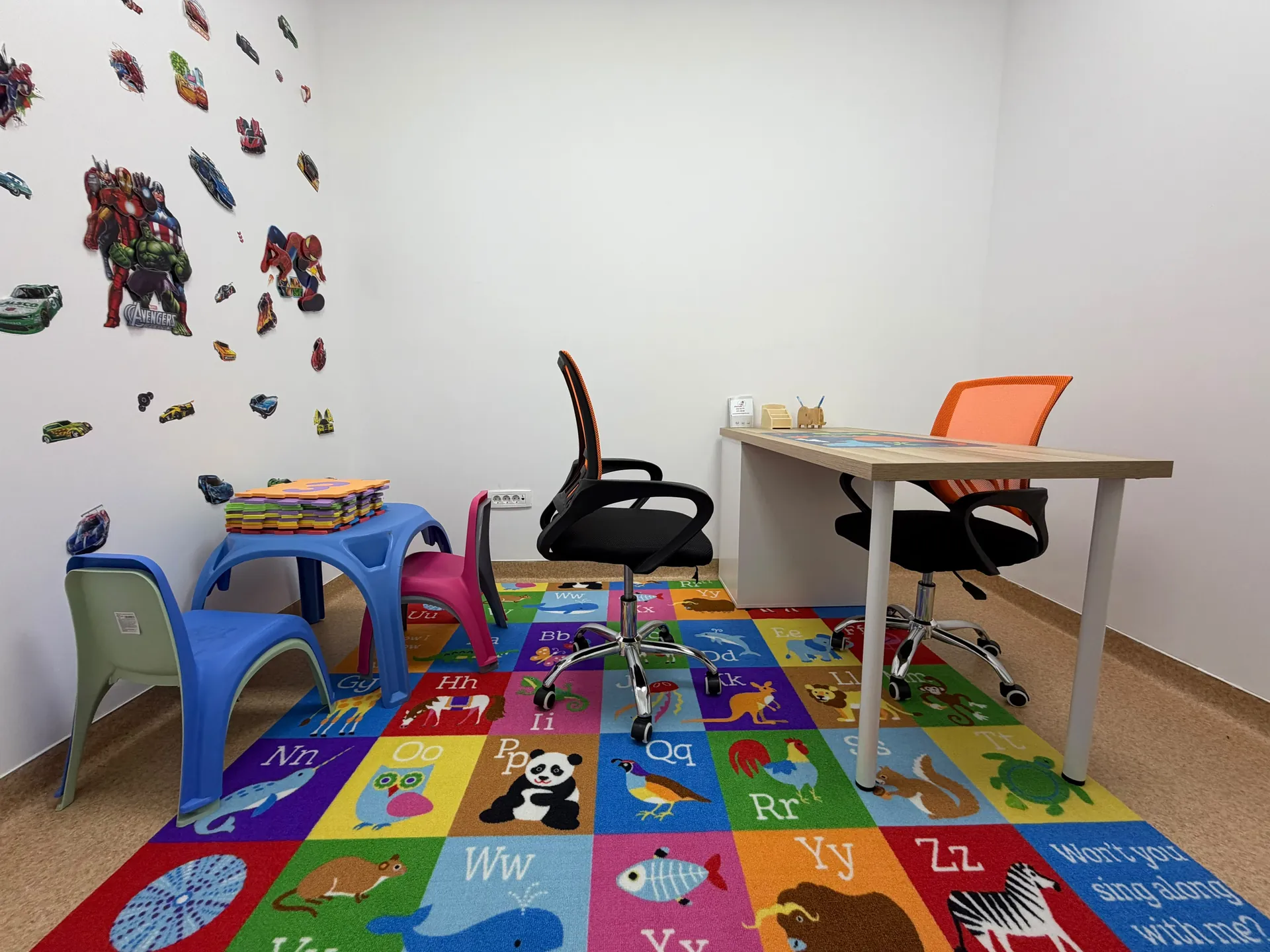A desk with two orange chairs, a children’s table and an animal-patterned rug.