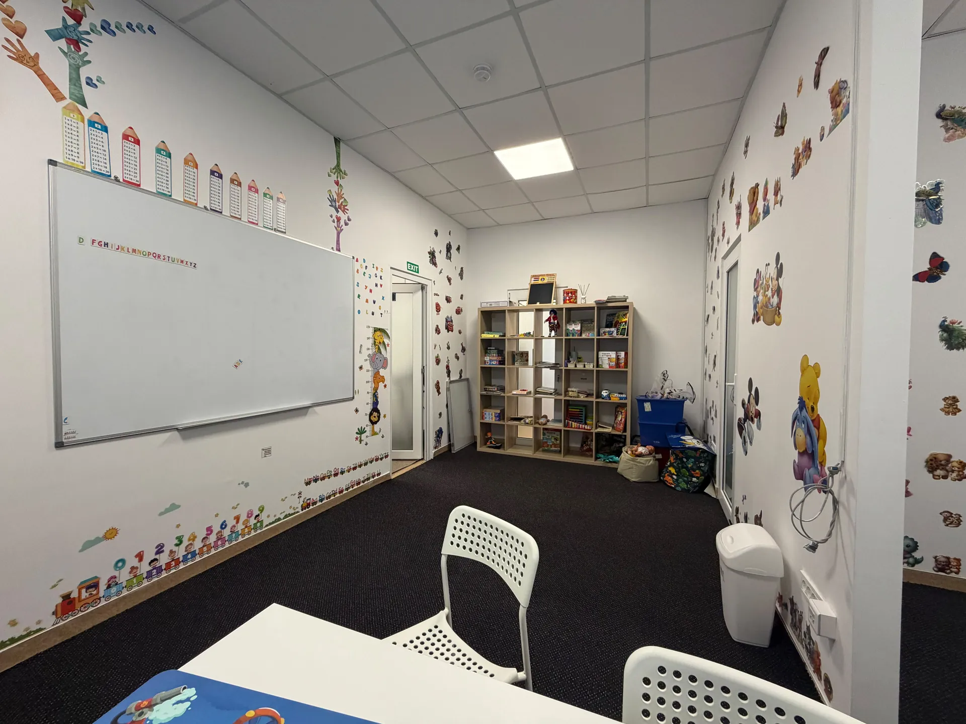 A whiteboard, letters, numbers and shelves of games in the activity room.