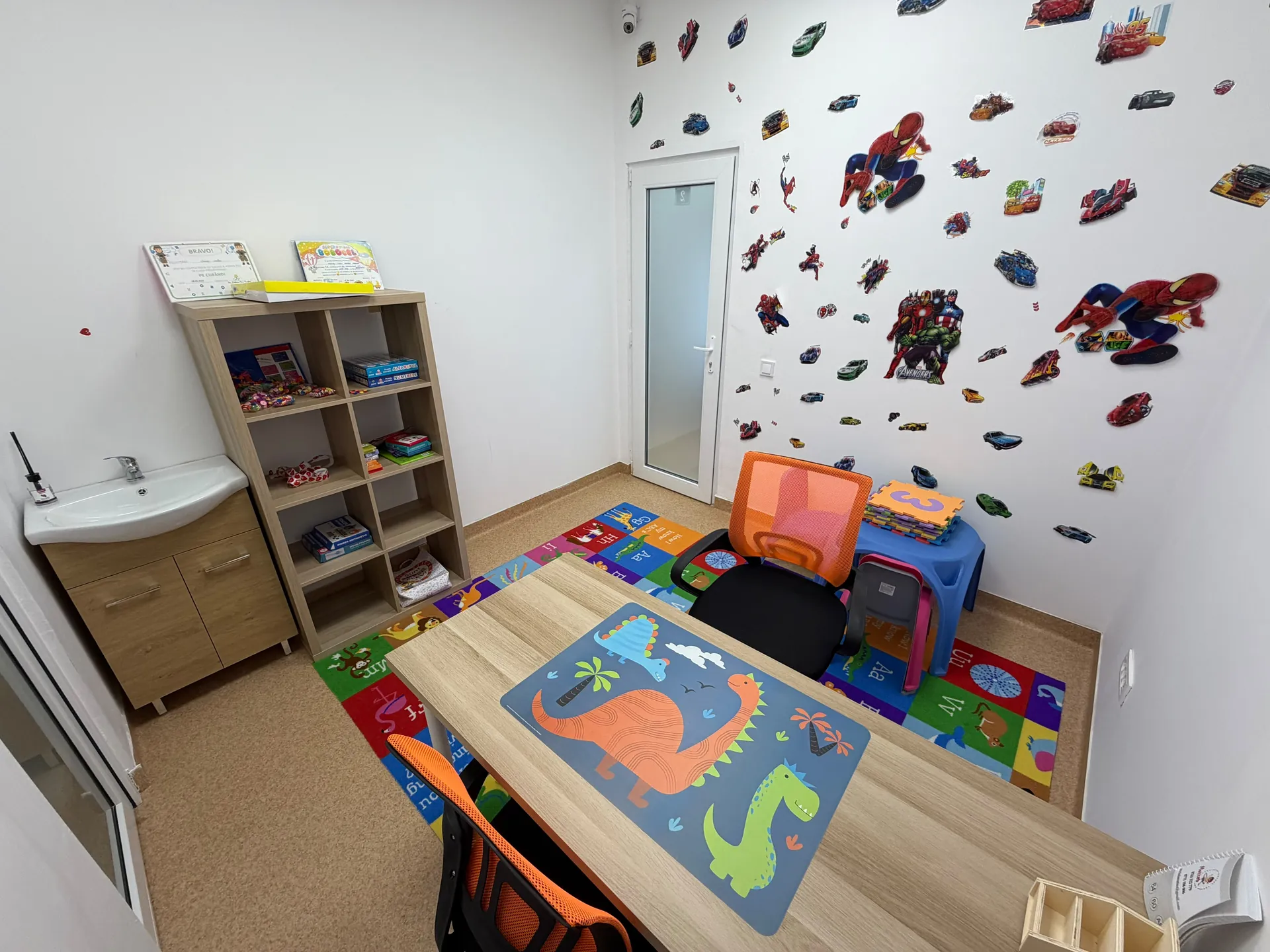 Shelves of games, a blue children’s table and a desk with a dinosaur mat.