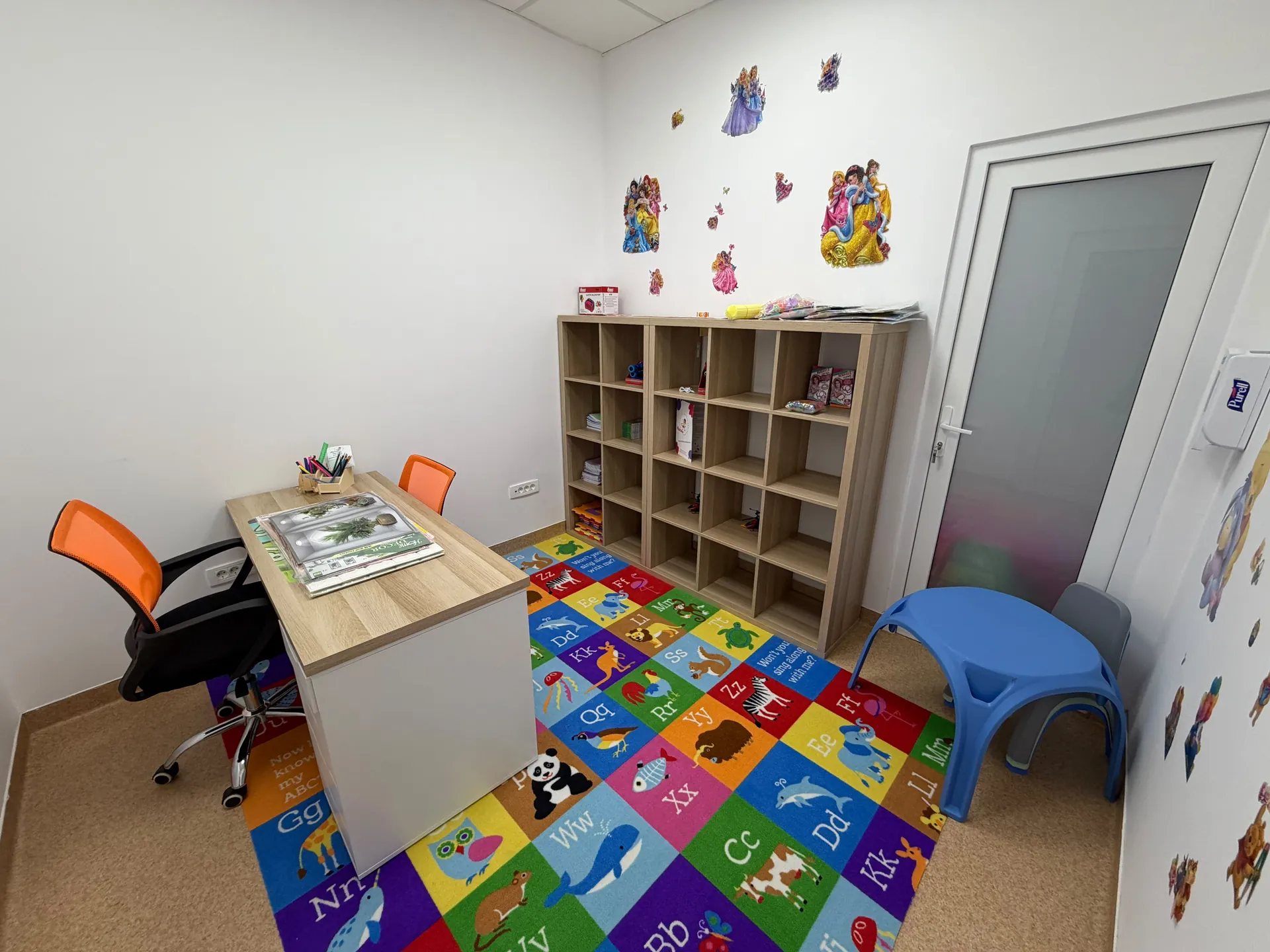 A room with a desk, open shelving and children’s furniture.